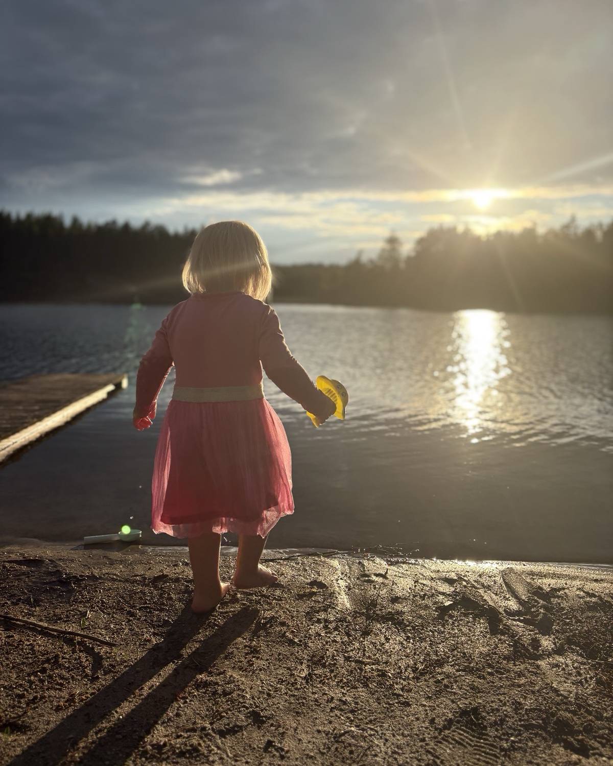 Pieni lapsi seisoo veden äärellä auringonlaskussa